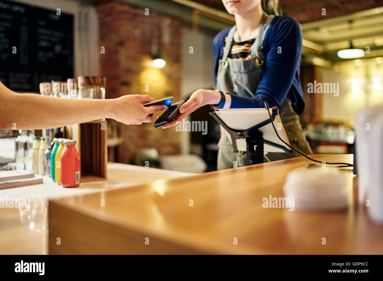 Female barista taking smartphone contactless payment from coffee shop customer Stock Photo