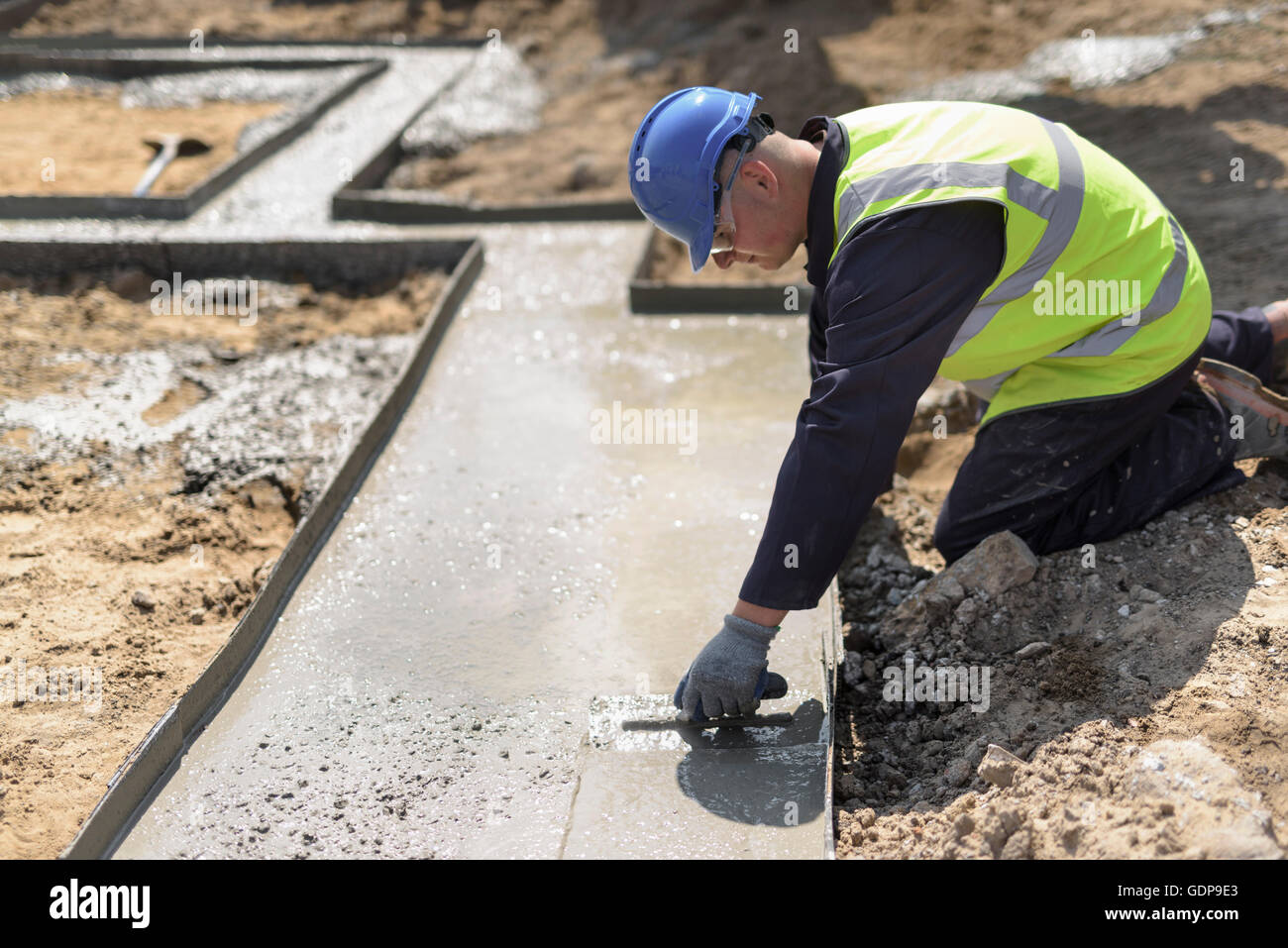Apprentice builder laying concrete foundations on building site Stock Photo