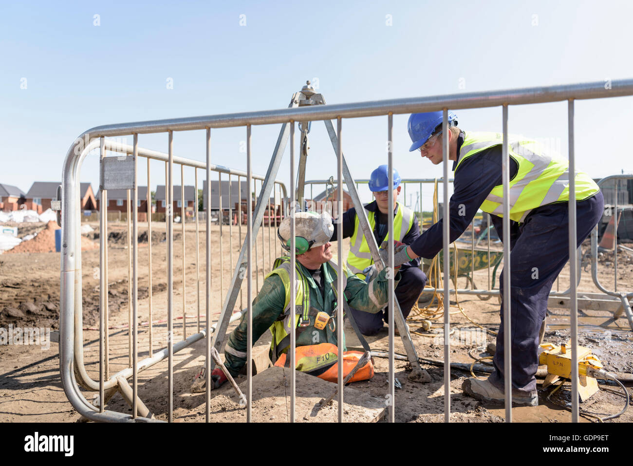Apprentice builders assisting worker out of manhole on building site Stock Photo