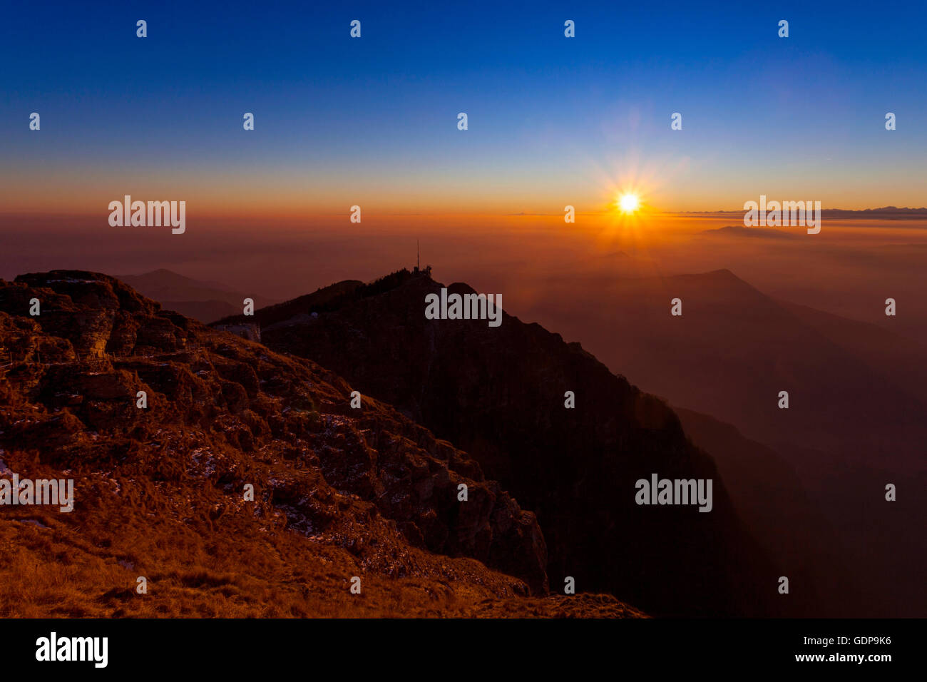 Elevated silhouetted landscape with valley mist at sunset, Monte Generoso,Ticino, Switzerland Stock Photo