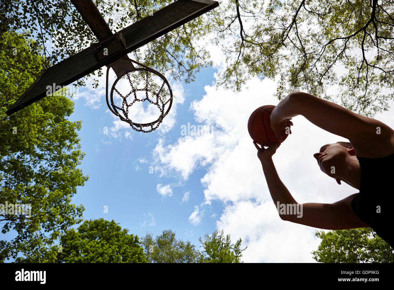 Low angle view of silhouetted young man aiming ball at basketball hoop Stock Photo