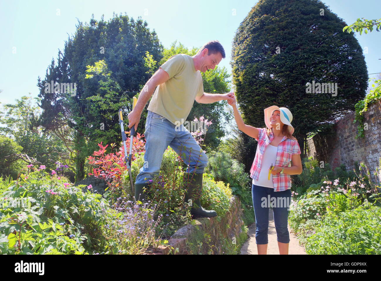 Woman in garden helping man stepping down from wall Stock Photo