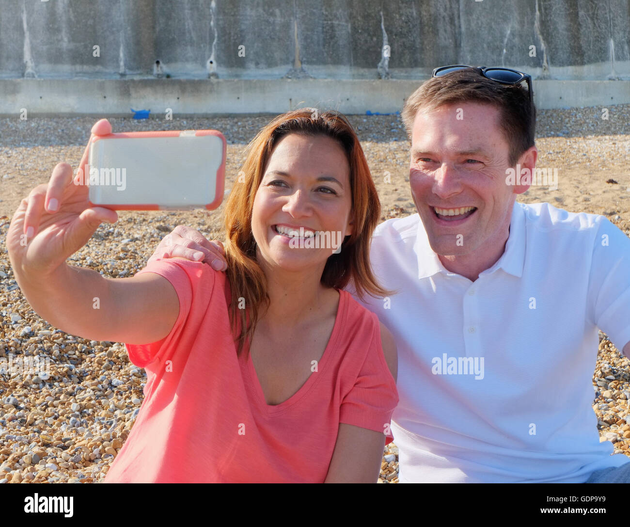 Couple taking selfie on shingle beach smiling Stock Photo