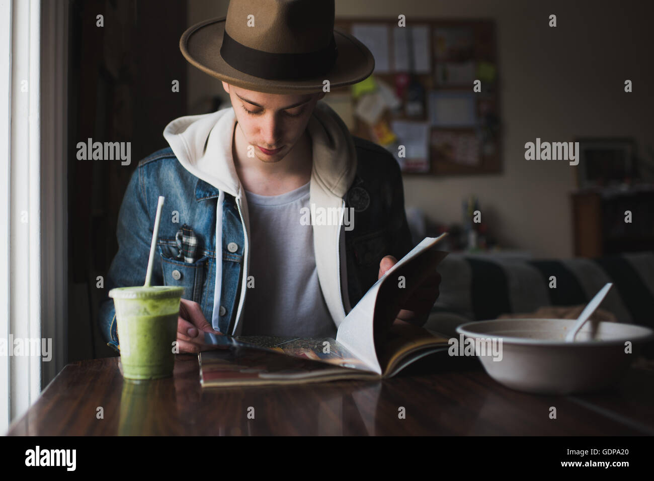 Young man sitting at table, having meal, reading magazine Stock Photo