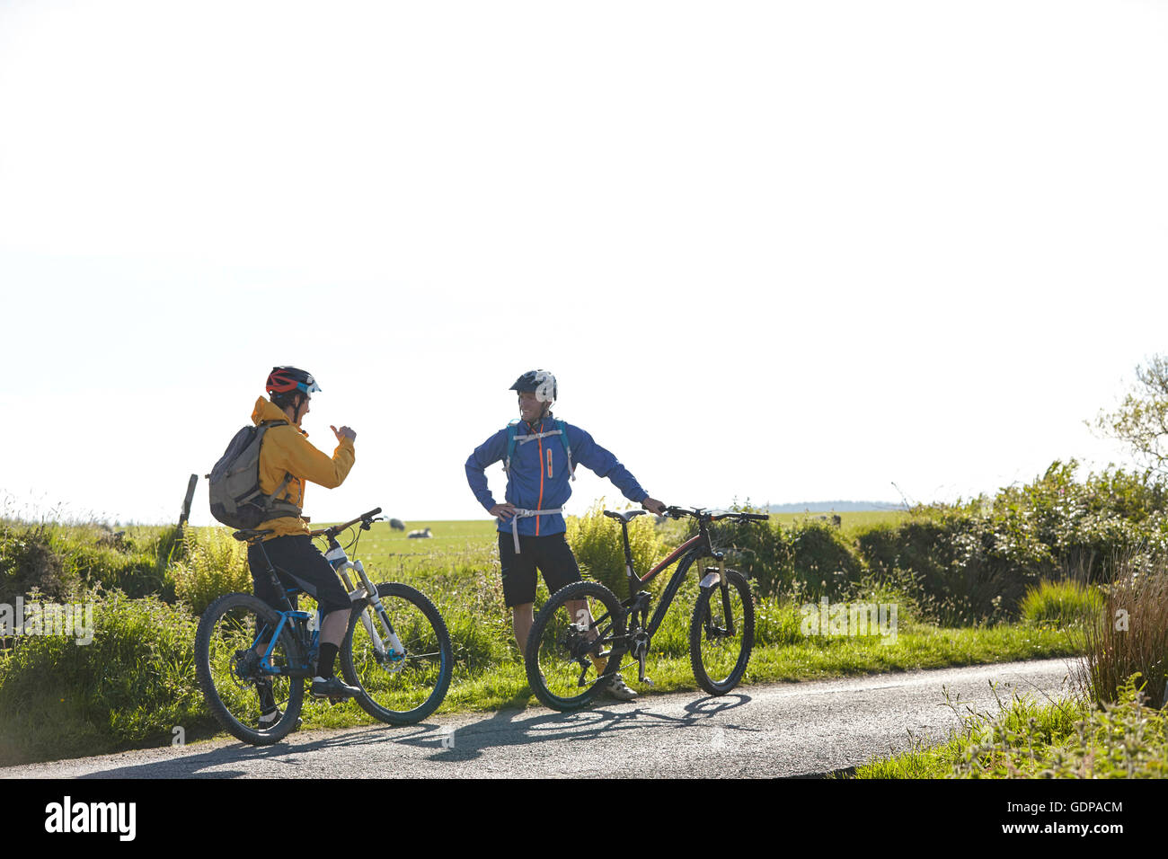 Cyclists holding bicycles on rural road chatting Stock Photo