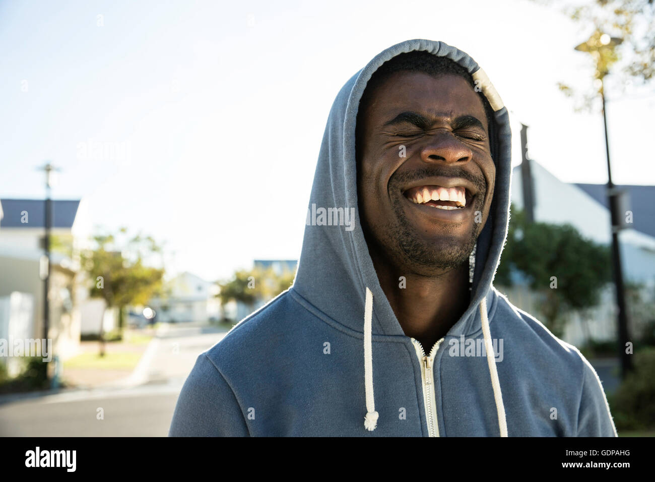 Portrait of man wearing hooded top eyes closed laughing Stock Photo