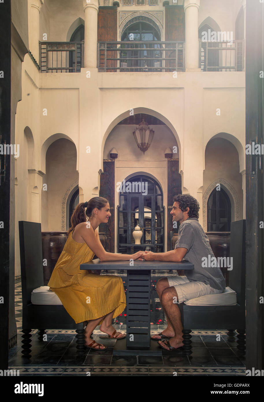 Side view of young couple at table face to face holding hands