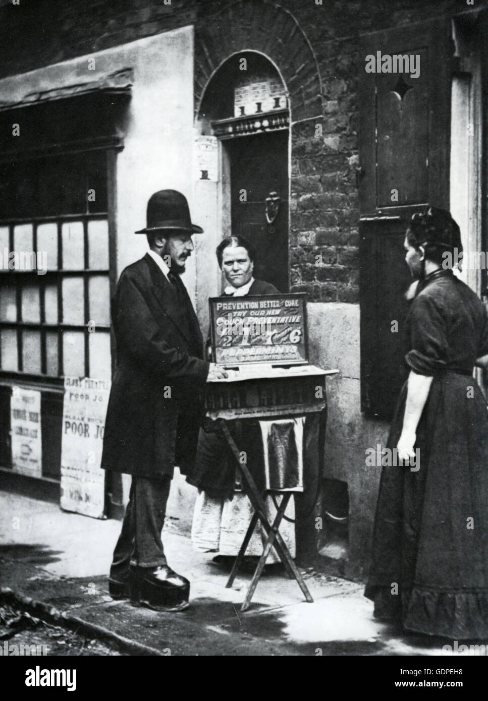 LONDON STREET PEDDLER in platform shoes shows off his cough medicines about 1862 in a poor area. The poster at left advertises a showing of 'Poor Joe' and other works by pioneering photographer Oscar Rejlander  at the Glass Theatre Stock Photo