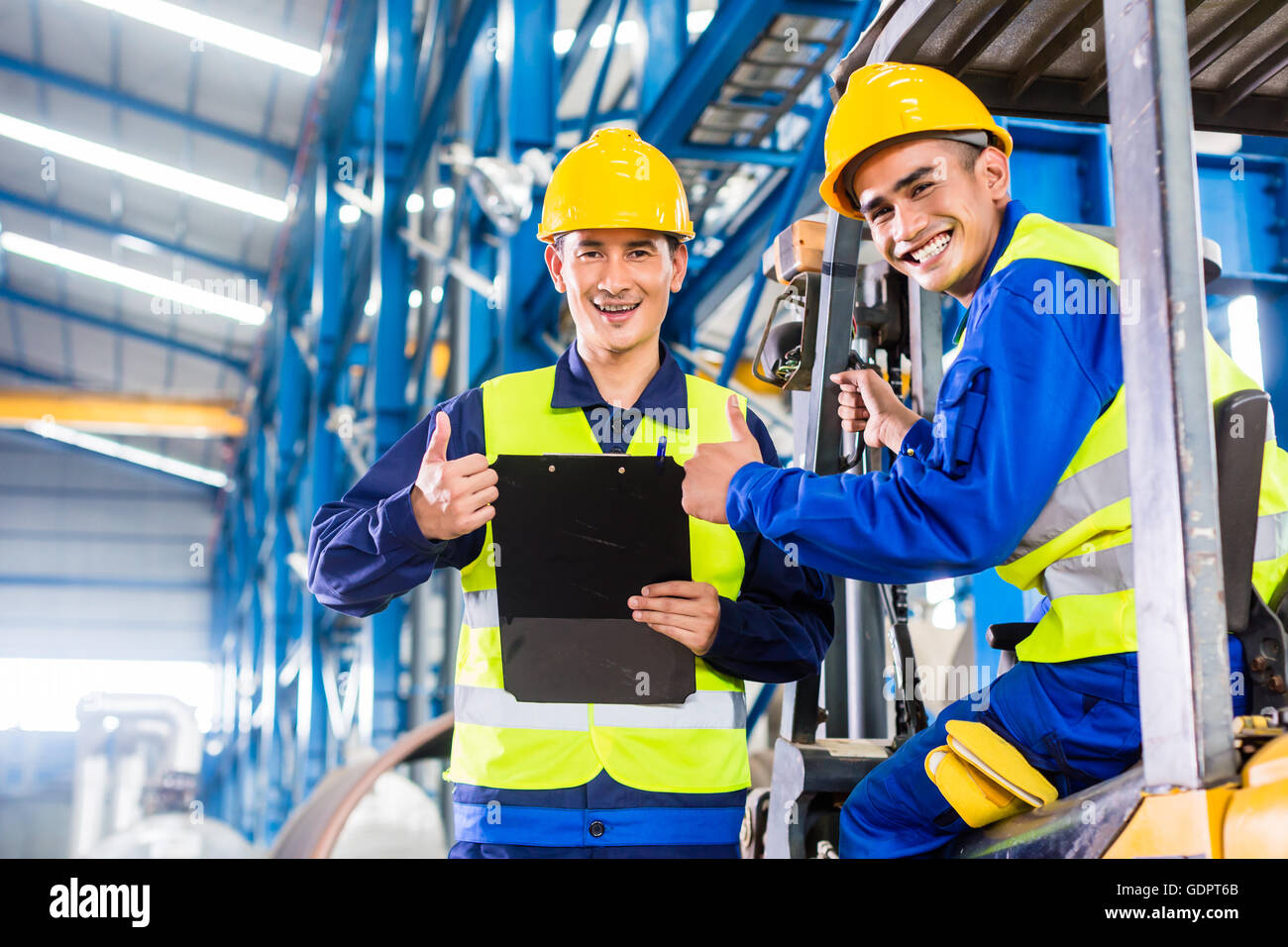 Worker and forklift driver in industrial factory looking at camera