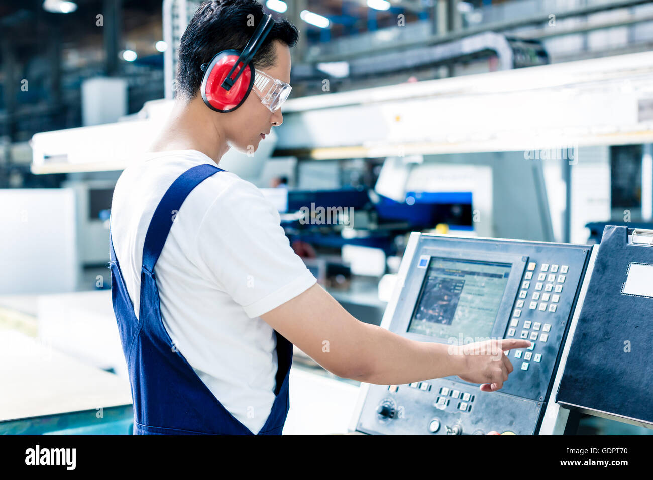 Worker entering data in CNC machine at factory floor to get the production going Stock Photo