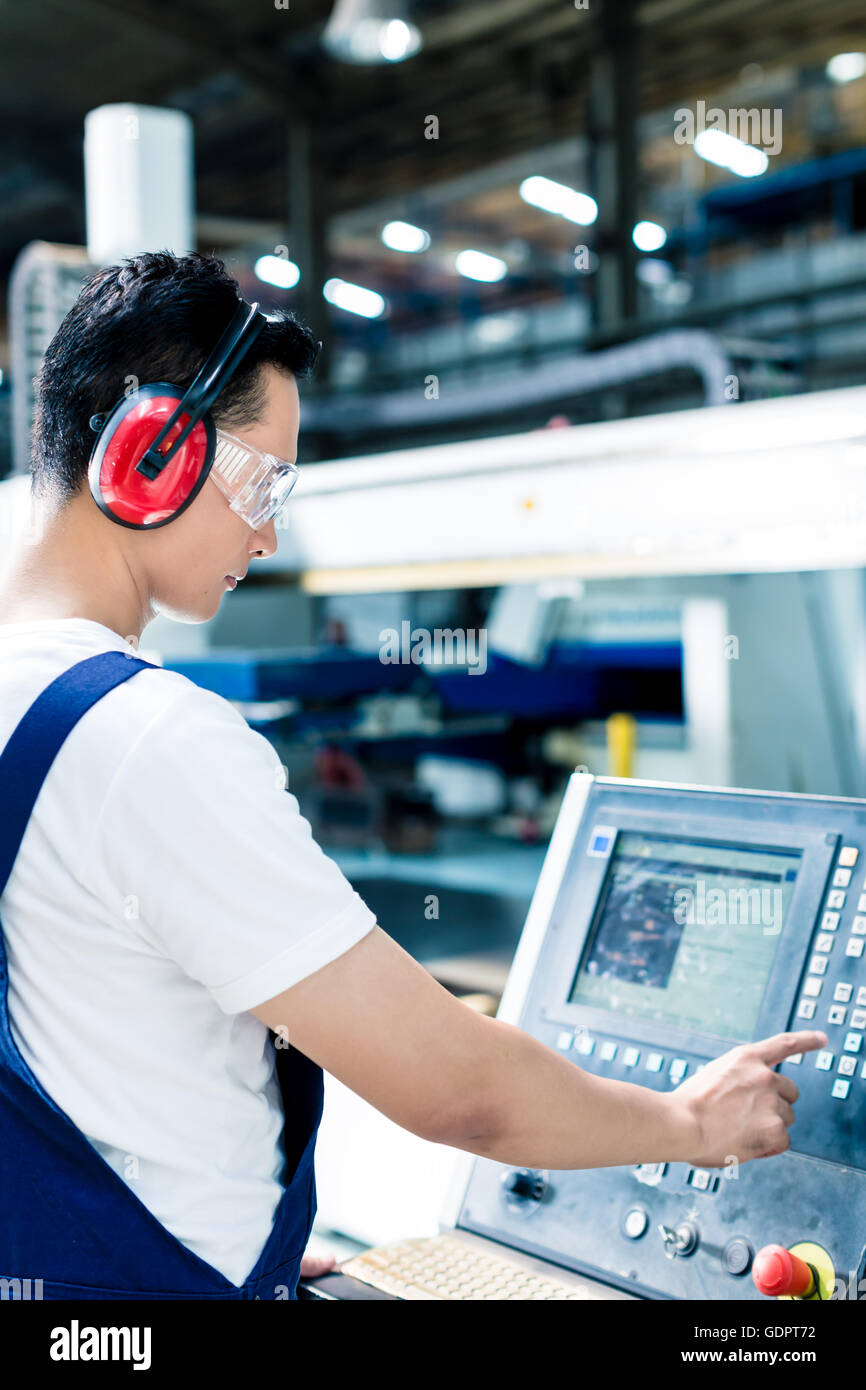 Worker entering data in CNC machine at factory floor to get the production going Stock Photo