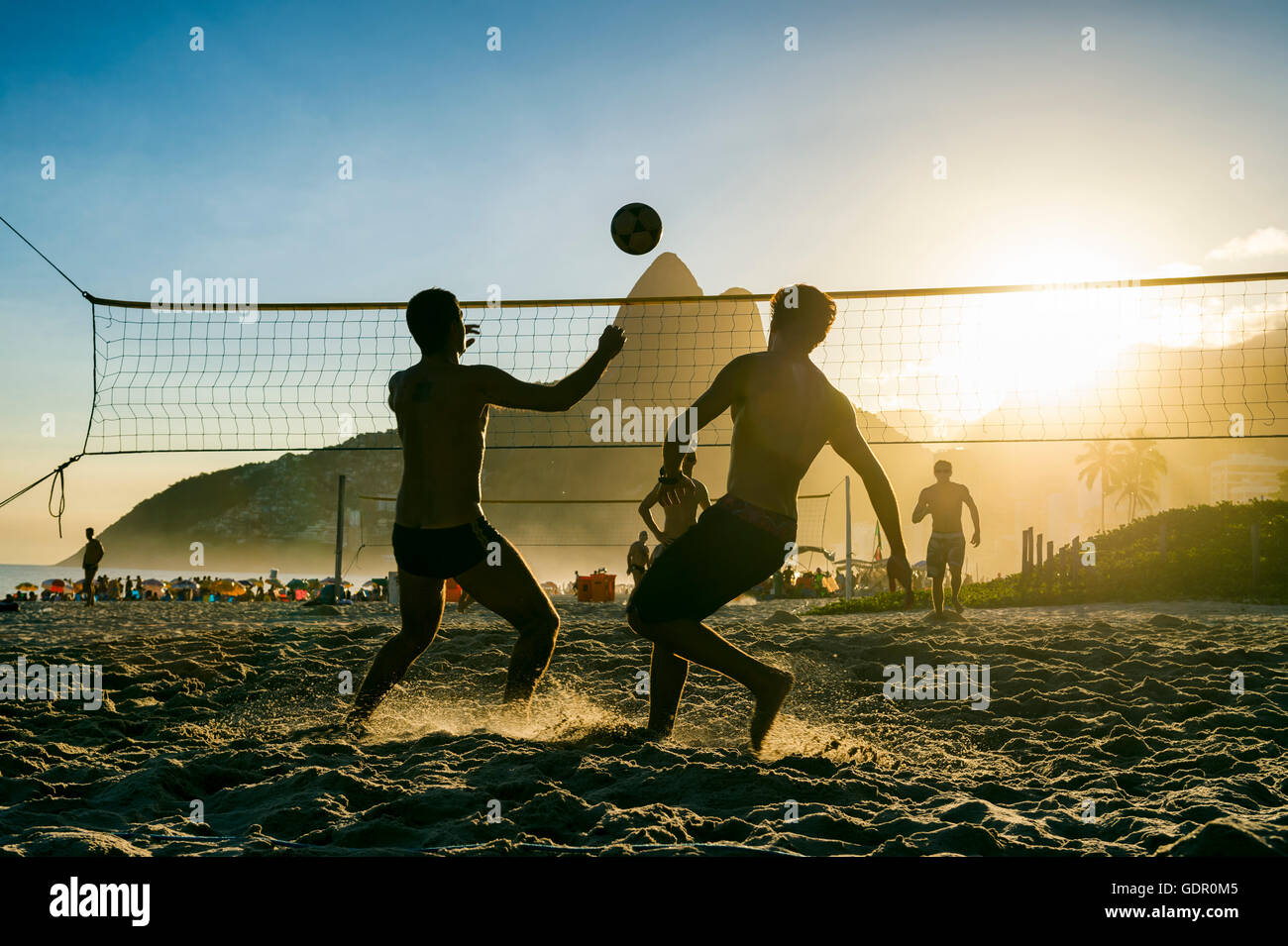 Silhouettes of Brazilians playing futevolei (footvolley) against a sunset backdrop of Two Brothers Mountain on Ipanema Beach Stock Photo