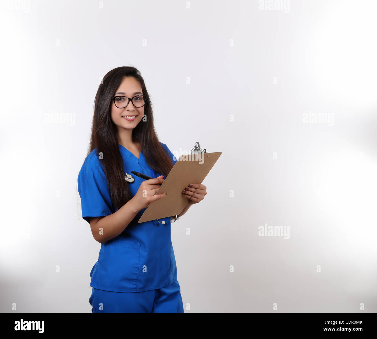 A young nurse wearing glasses takes notes on her clip board. Stock Photo