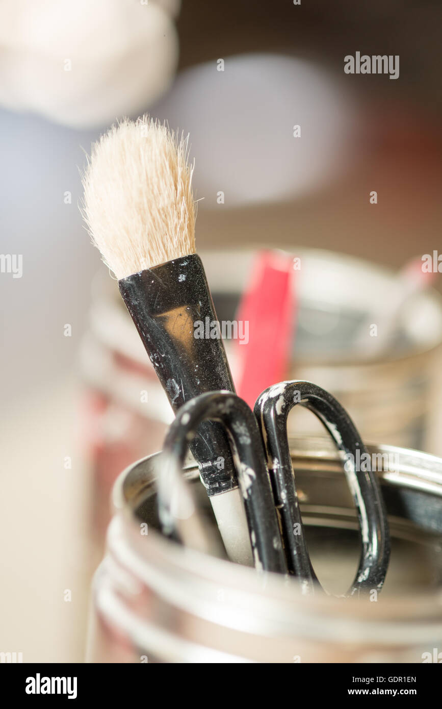 Close-up of a used paint brush with worn bristles and a pair of