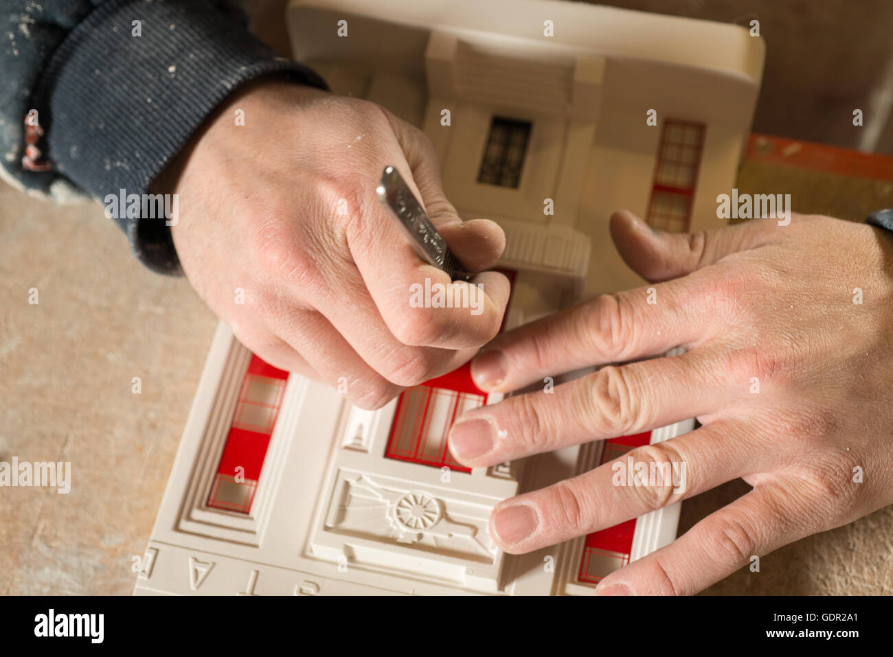 Hands, one holding a metal object, working on a plaster scale model architectural building Stock Photo