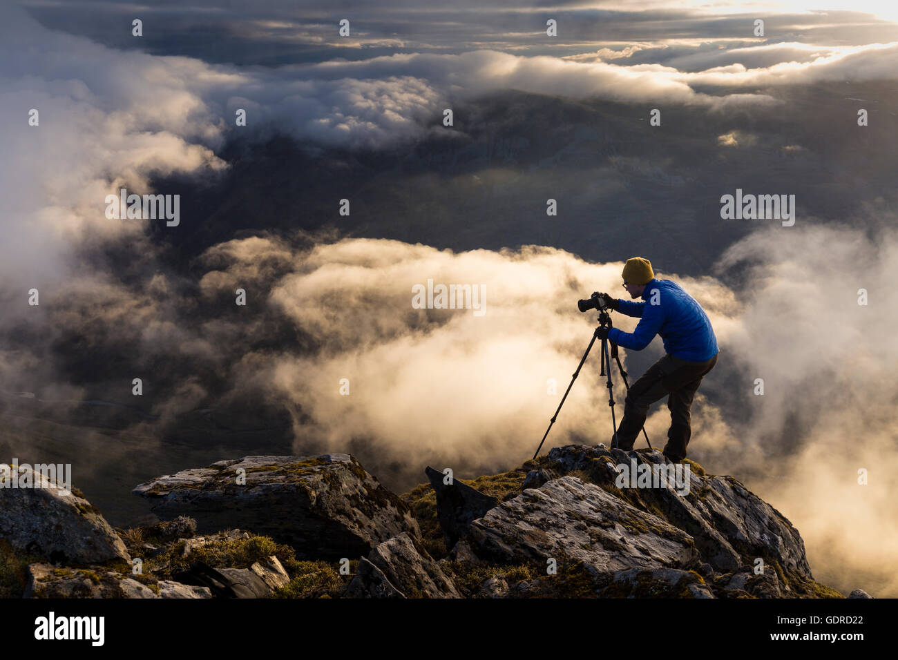 A landscape photographer setting up for his shot above the clouds on a steep cliff in the Scottish Highlands (Kintail) Stock Photo