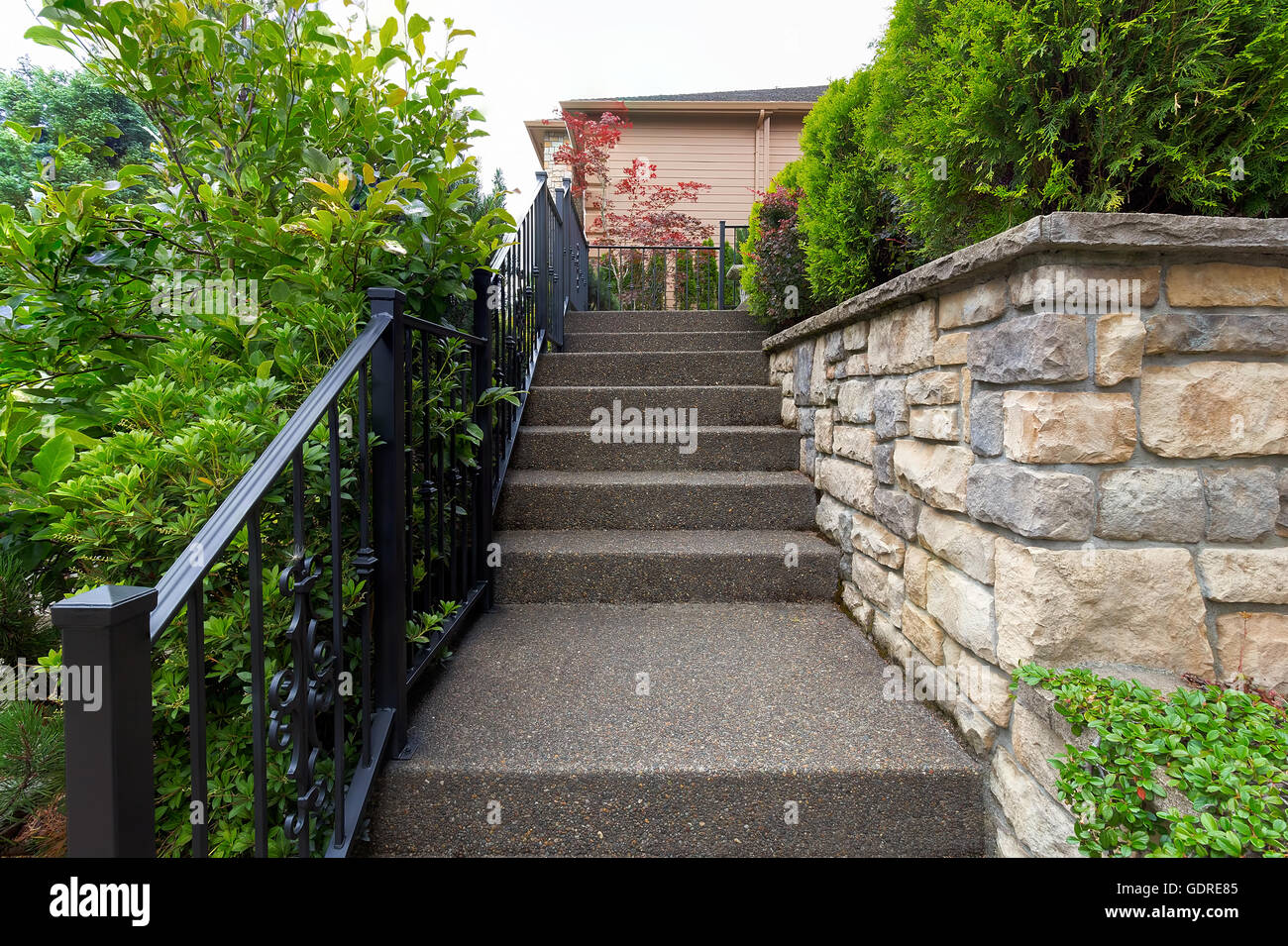Outdoor stairs with wrought iron black railings stone facade planters and cement steps to house front door entrance Stock Photo