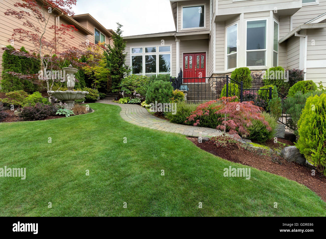 Frontyard garden of house with water fountain green grass lawn paver brick path trees and shrubs landscaping Stock Photo