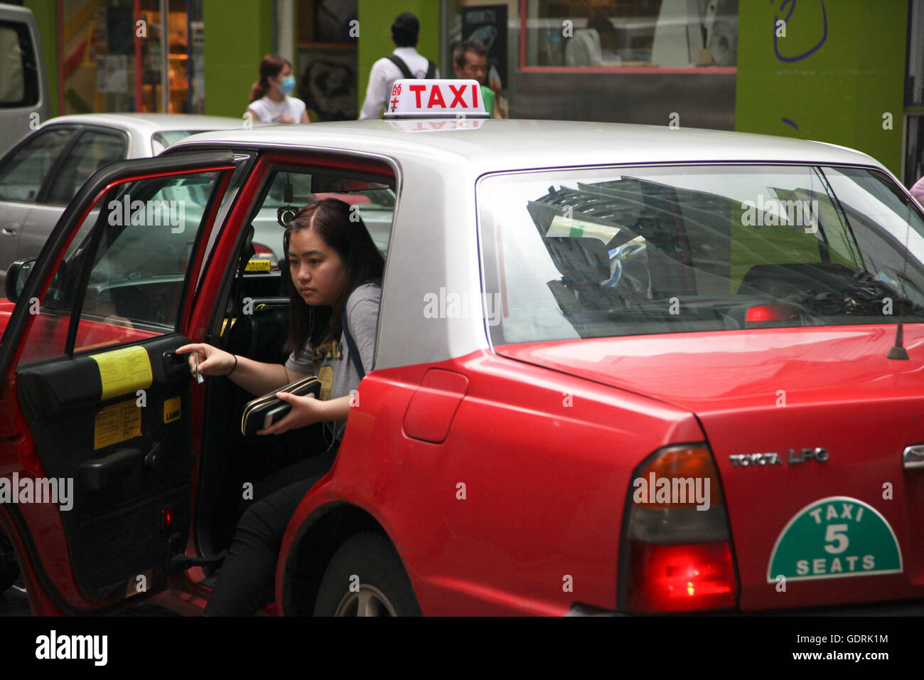 A woman getting out of a red Hong Kong taxi in Central District of Hong Kong. Stock Photo
