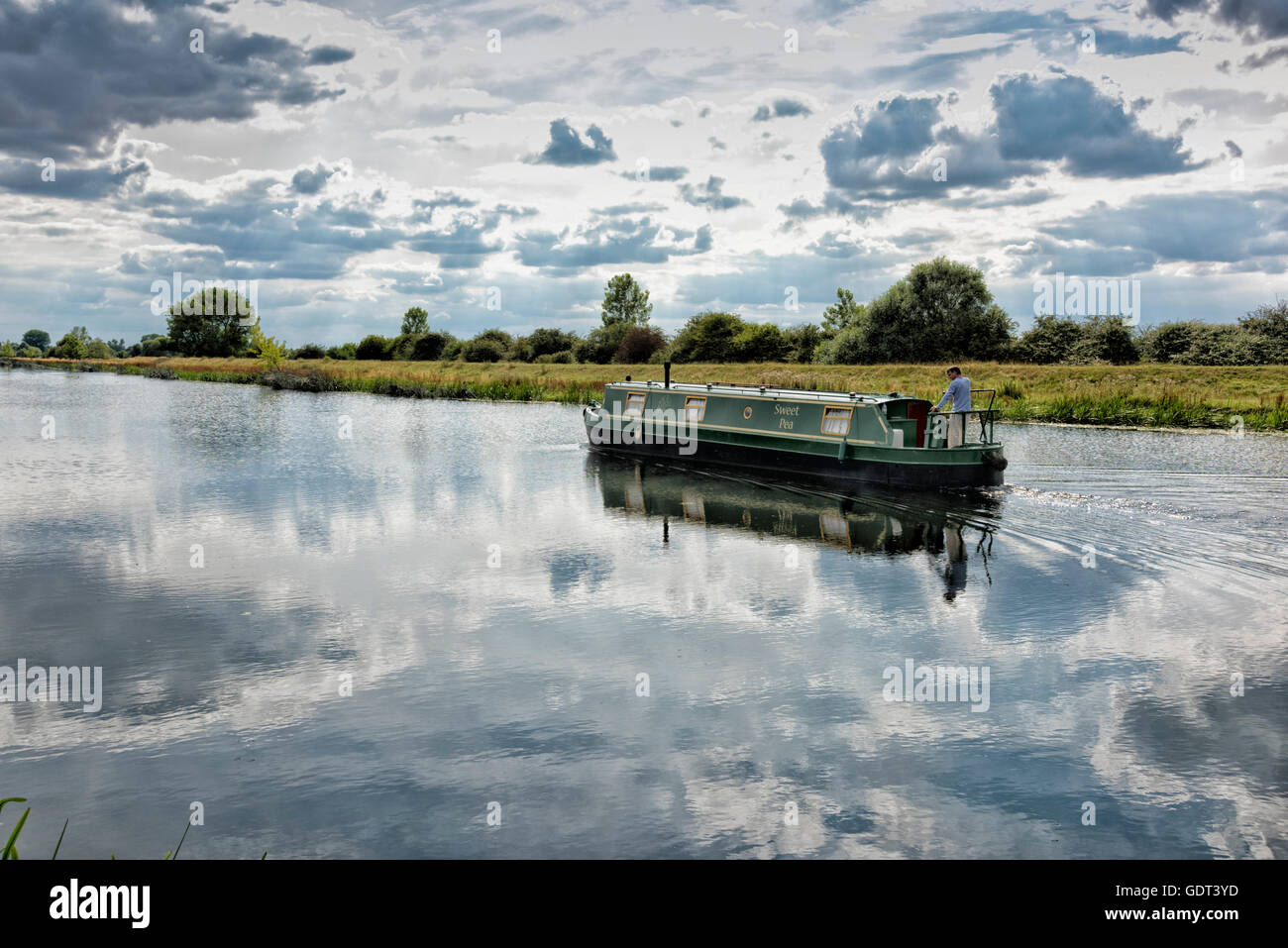 River Great Ouse, Over, Cambridgeshire, UK 21st July 2016. A narrowboat glides along the river on a hot and humid afternoon. The hot weather continues and temperatures reached around 26 degrees centigrade even though there was considerable cloud cover. Credit Julian Eales/Alamy Live news Stock Photo