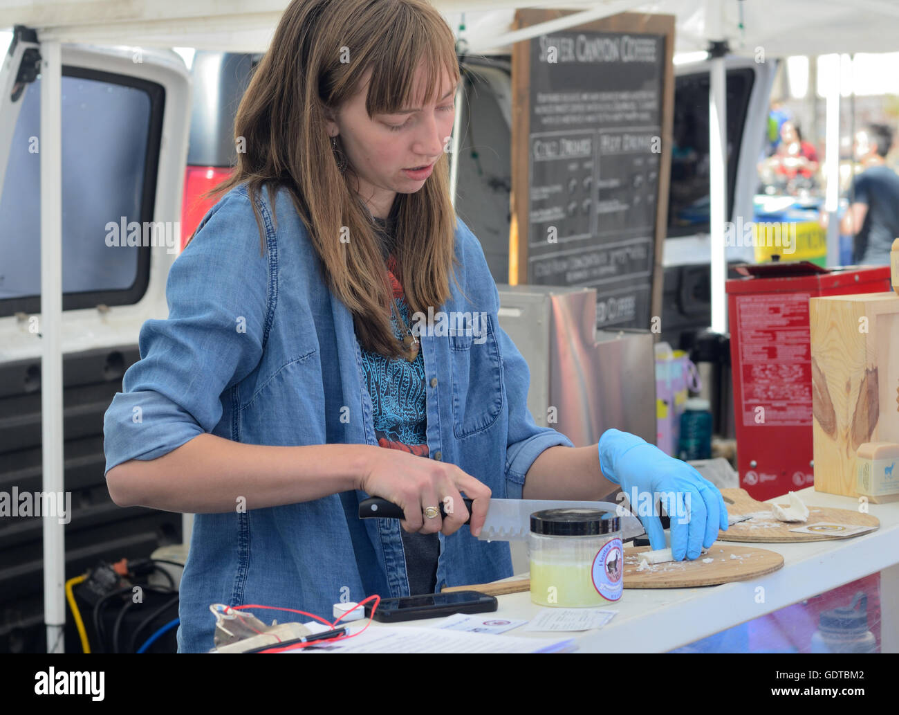Worker at a booth at the Boulder Farmers Market slizes samples of cheese. Stock Photo