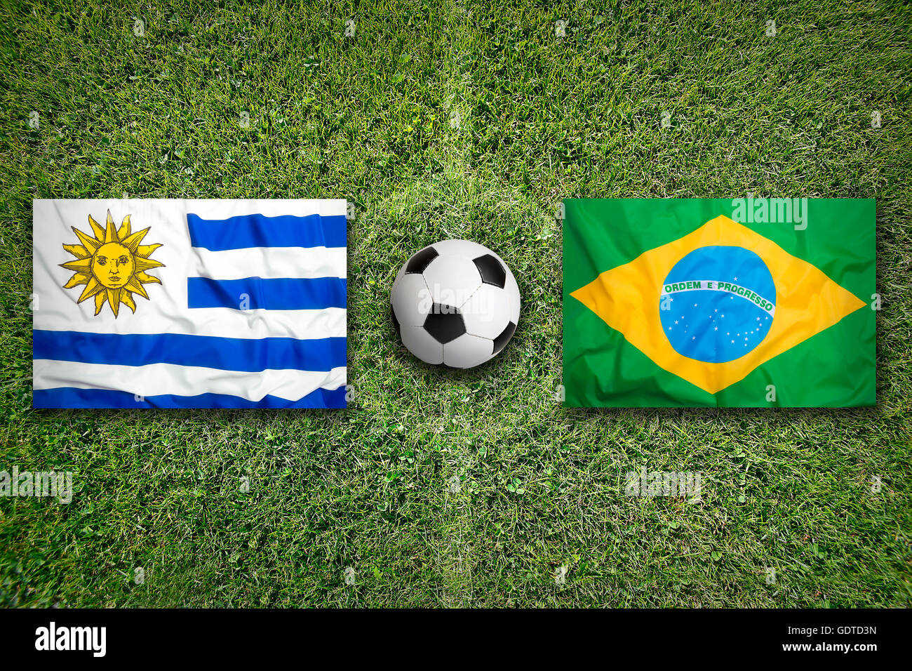 Uruguay vs. Brazil flags on green soccer field Stock Photo