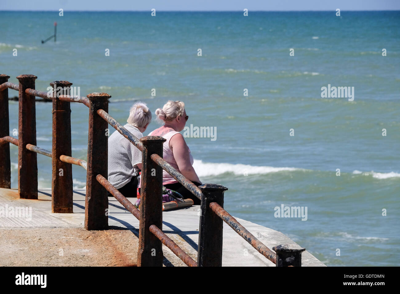 Two people sat on sea wall looking out to sea Stock Photo