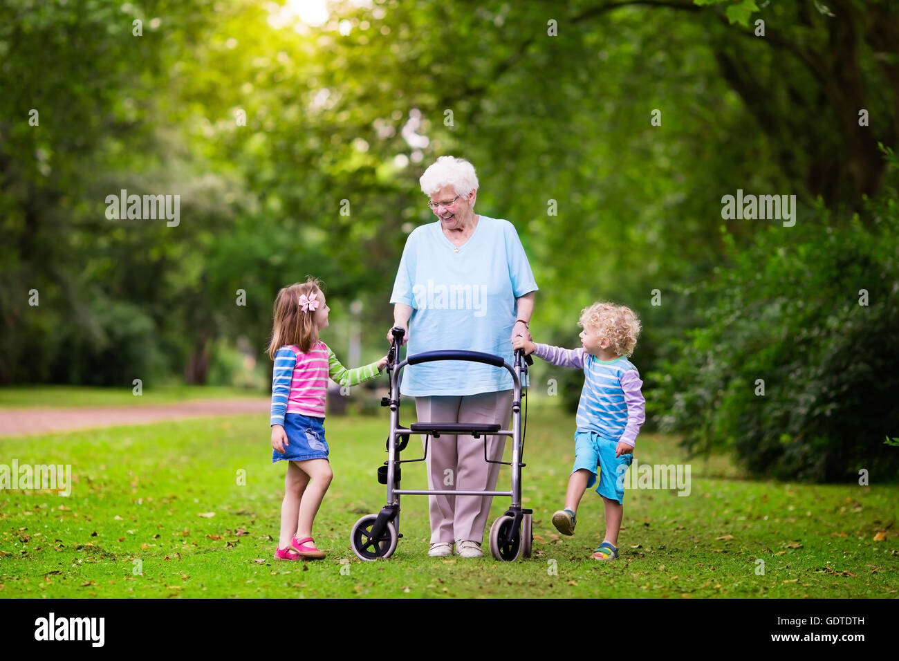 Happy senior lady playing with little boy and girl in blooming rose garden. Grandmother with grand children sitting on a bench Stock Photo