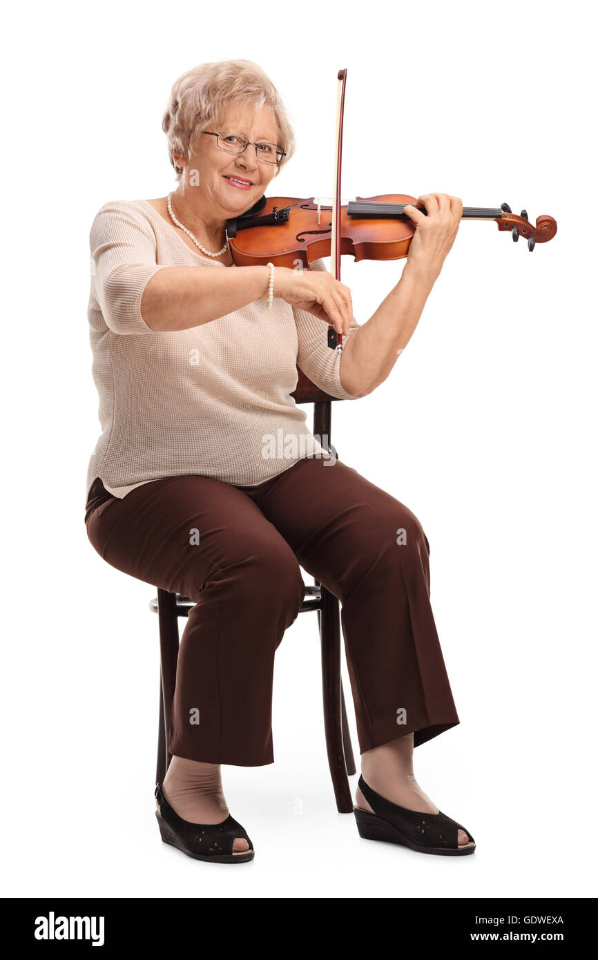 Vertical shot of a mature female violinist playing a violin seated on a chair isolated on white background Stock Photo
