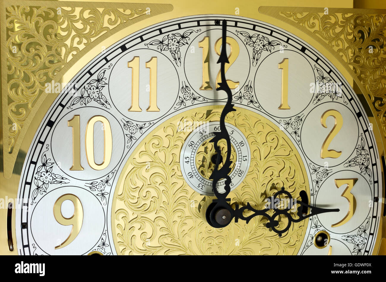 ornate brass engraved grandfather clock face with arabic numerals and hands on three o'clock Stock Photo