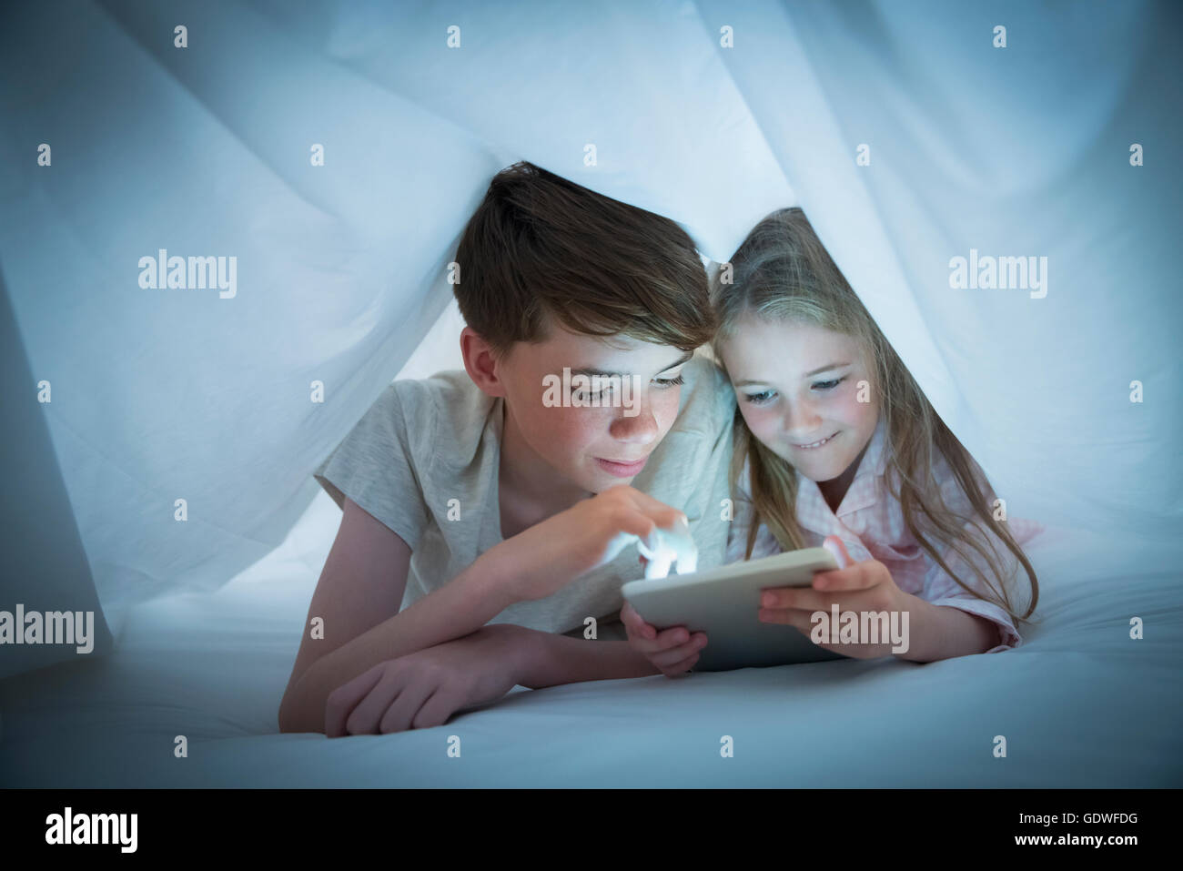 Brother and sister sharing digital tablet under sheet Stock Photo