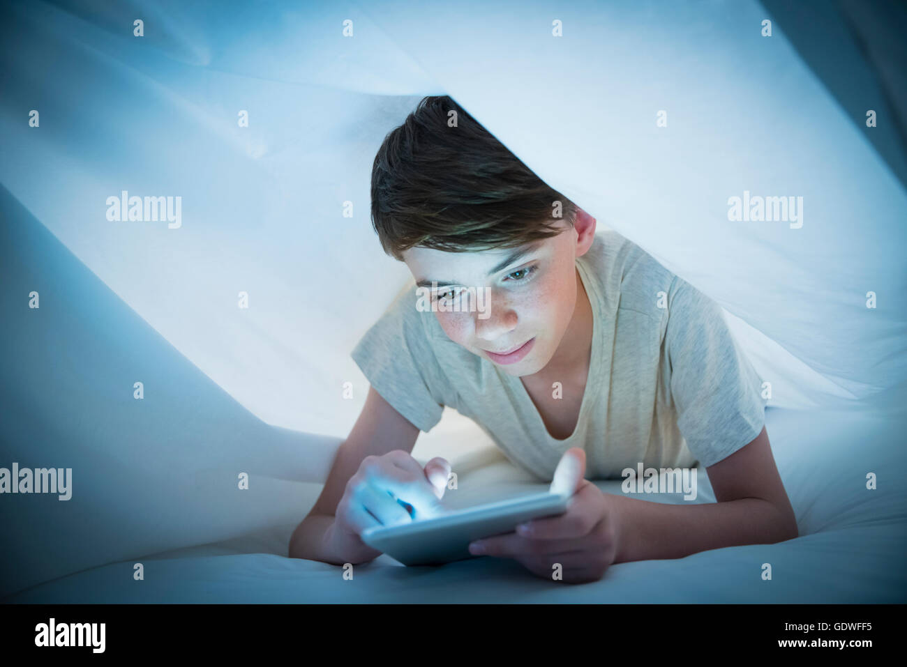 Boy using digital tablet under sheet Stock Photo
