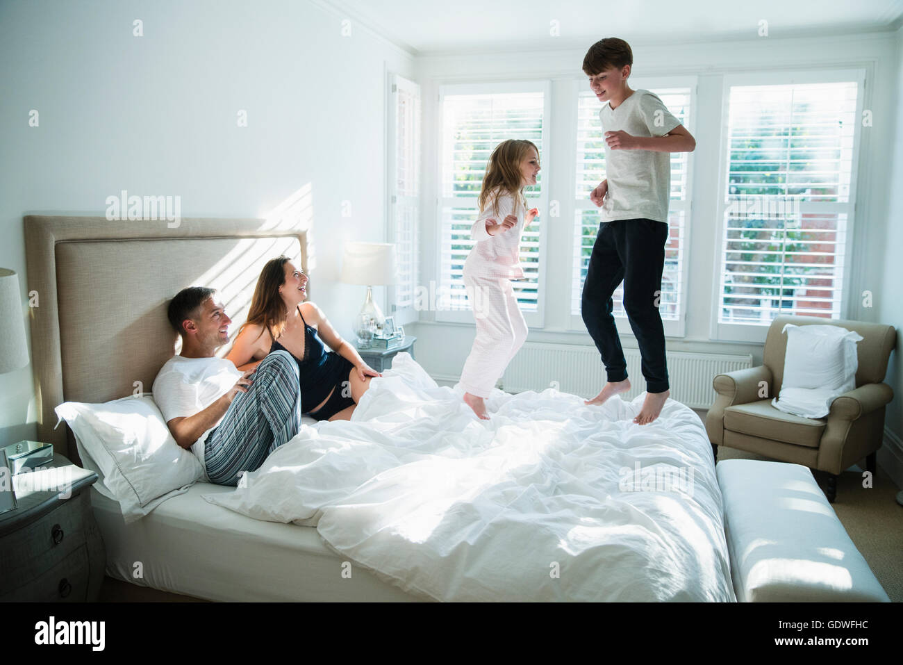 Parents watching children jumping on bed Stock Photo