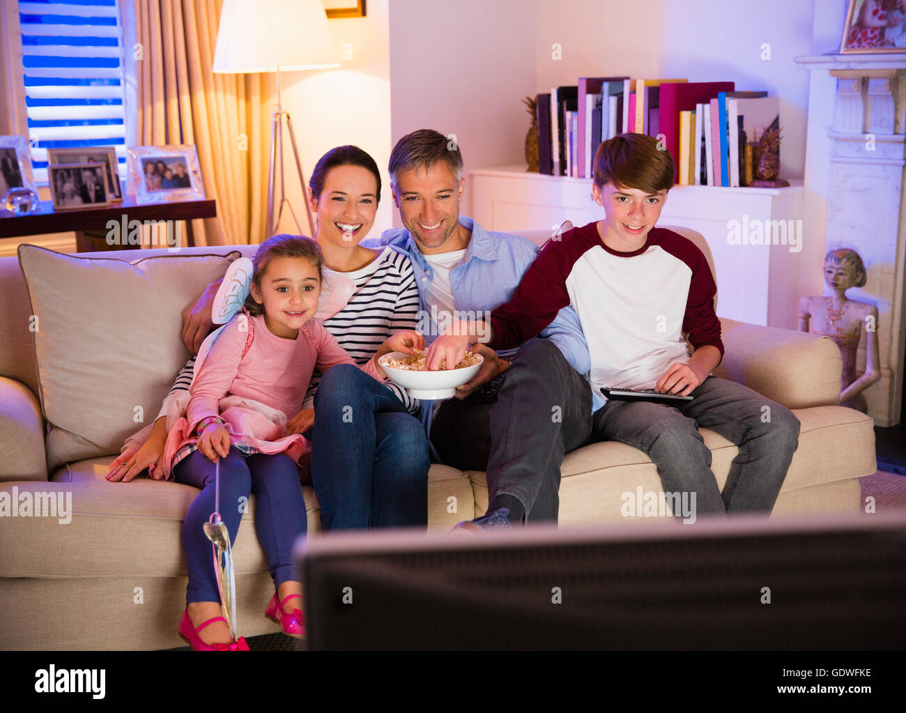 Family eating popcorn and watching TV in living room Stock Photo