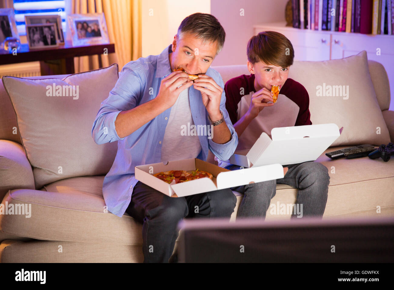 Father and son eating pizza and watching TV in living room Stock Photo