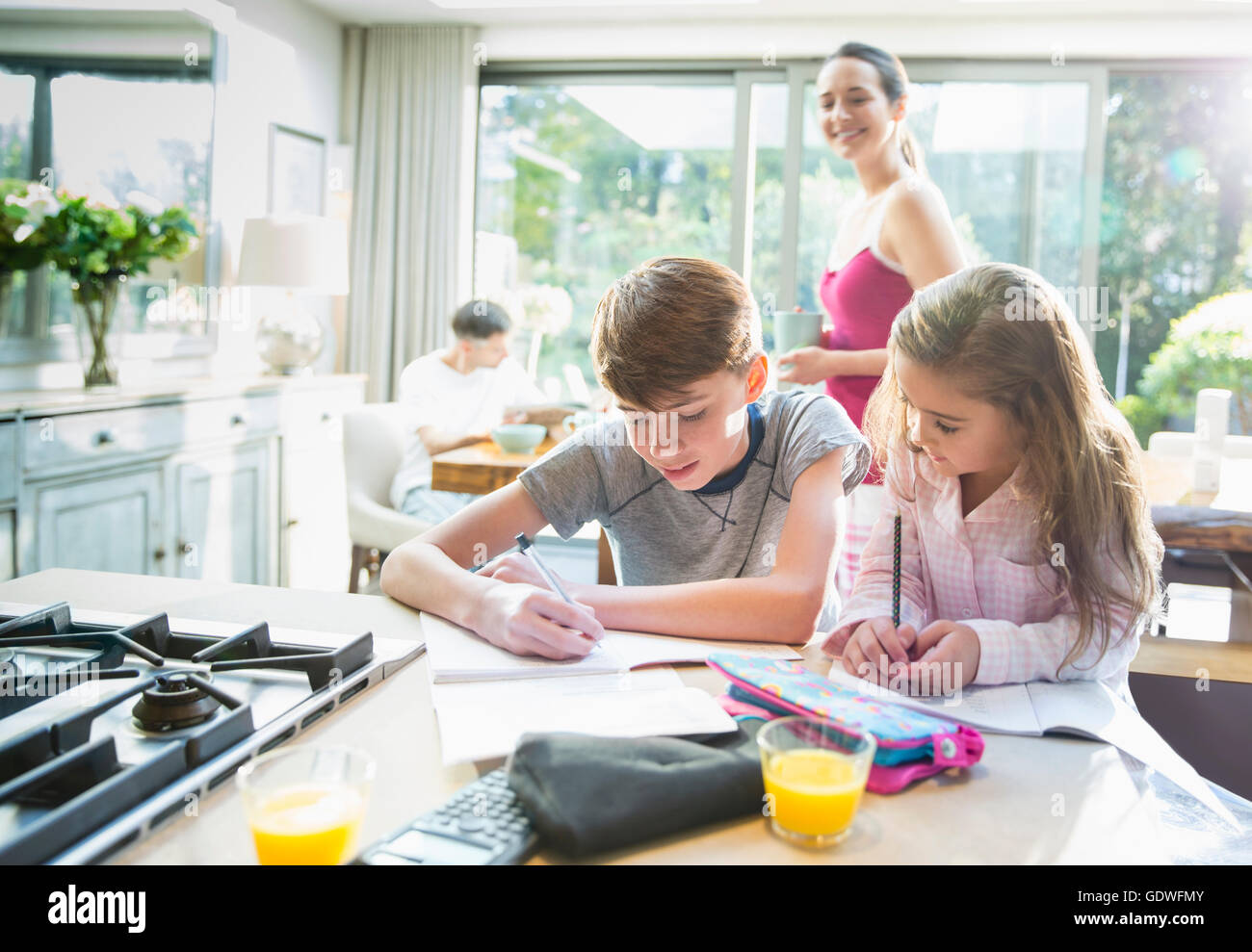 Mother watching brother and sister doing homework at kitchen counter Stock Photo
