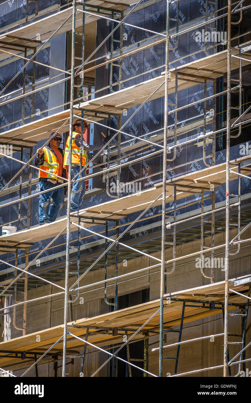 Two workers in bright safety vests standing on scaffolding of tall ...