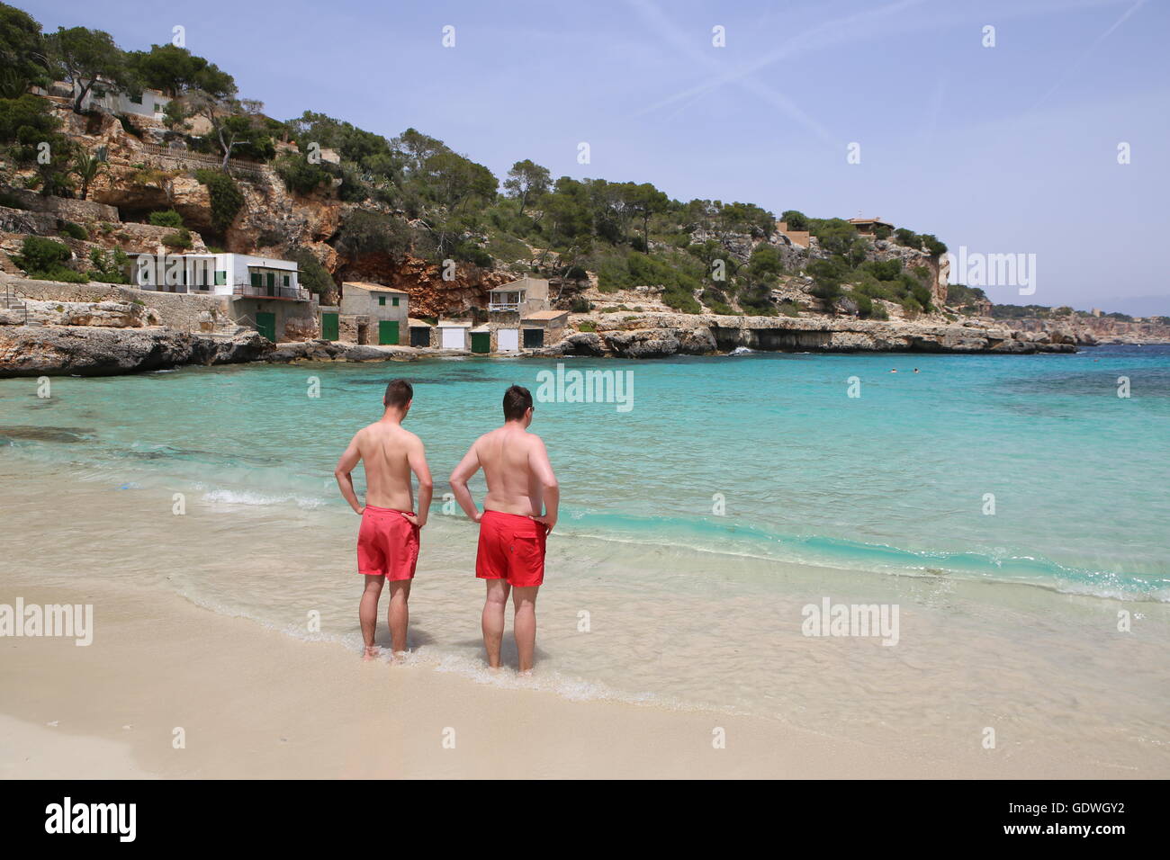 Two boys with the same red swimsuit looking at the sea in the beautiful Cala Llombards, south of Mallorca Stock Photo