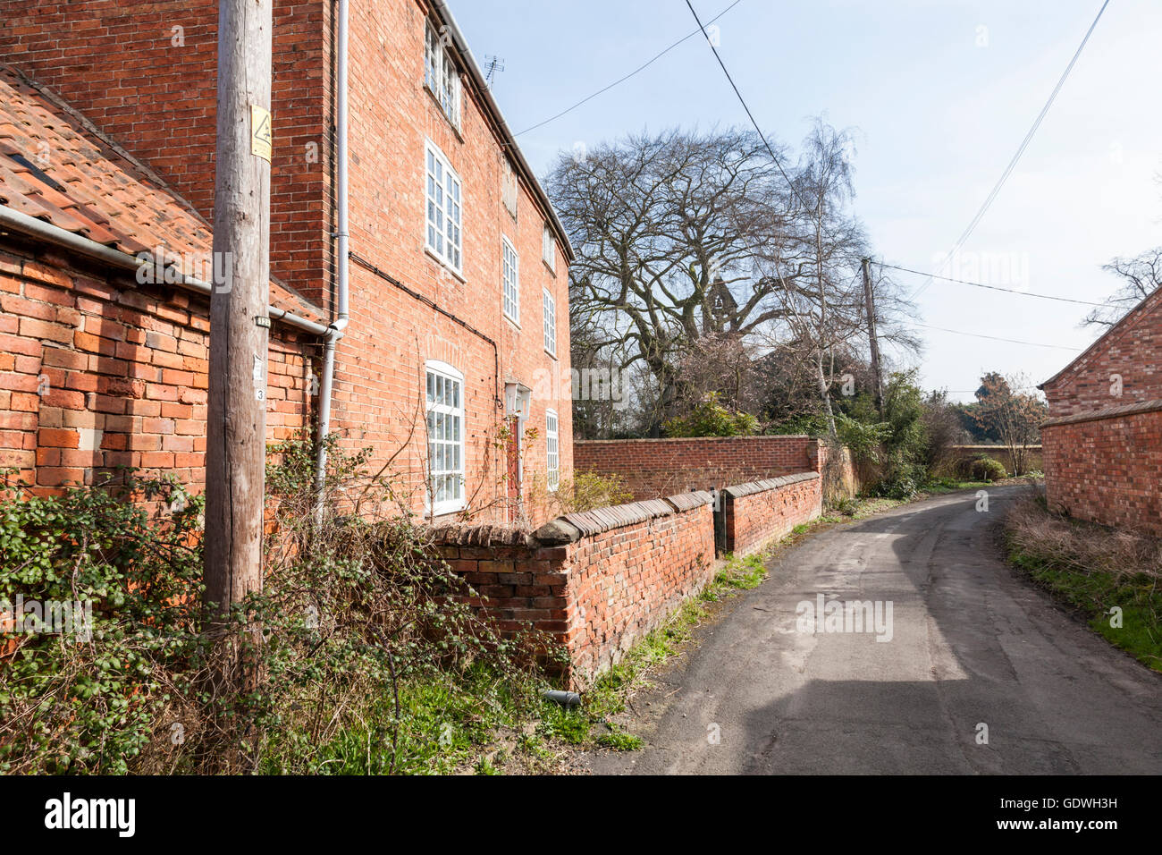 Red brick cottage and other buildings on an old narrow village lane, Costock, Nottinghamshire, England, UK Stock Photo