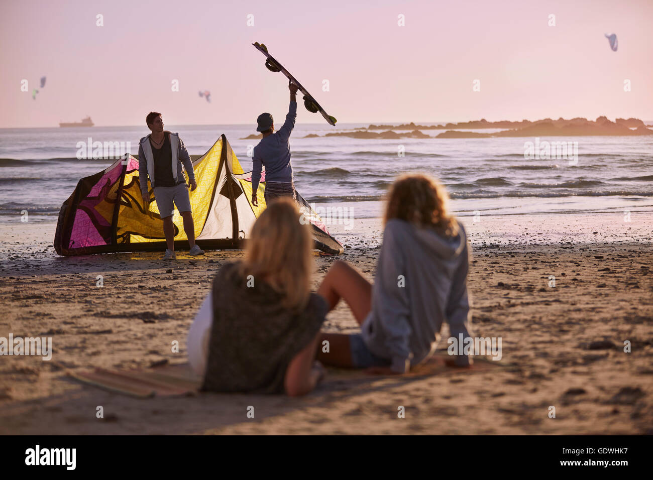 Women watching men preparing to kiteboard on beach Stock Photo