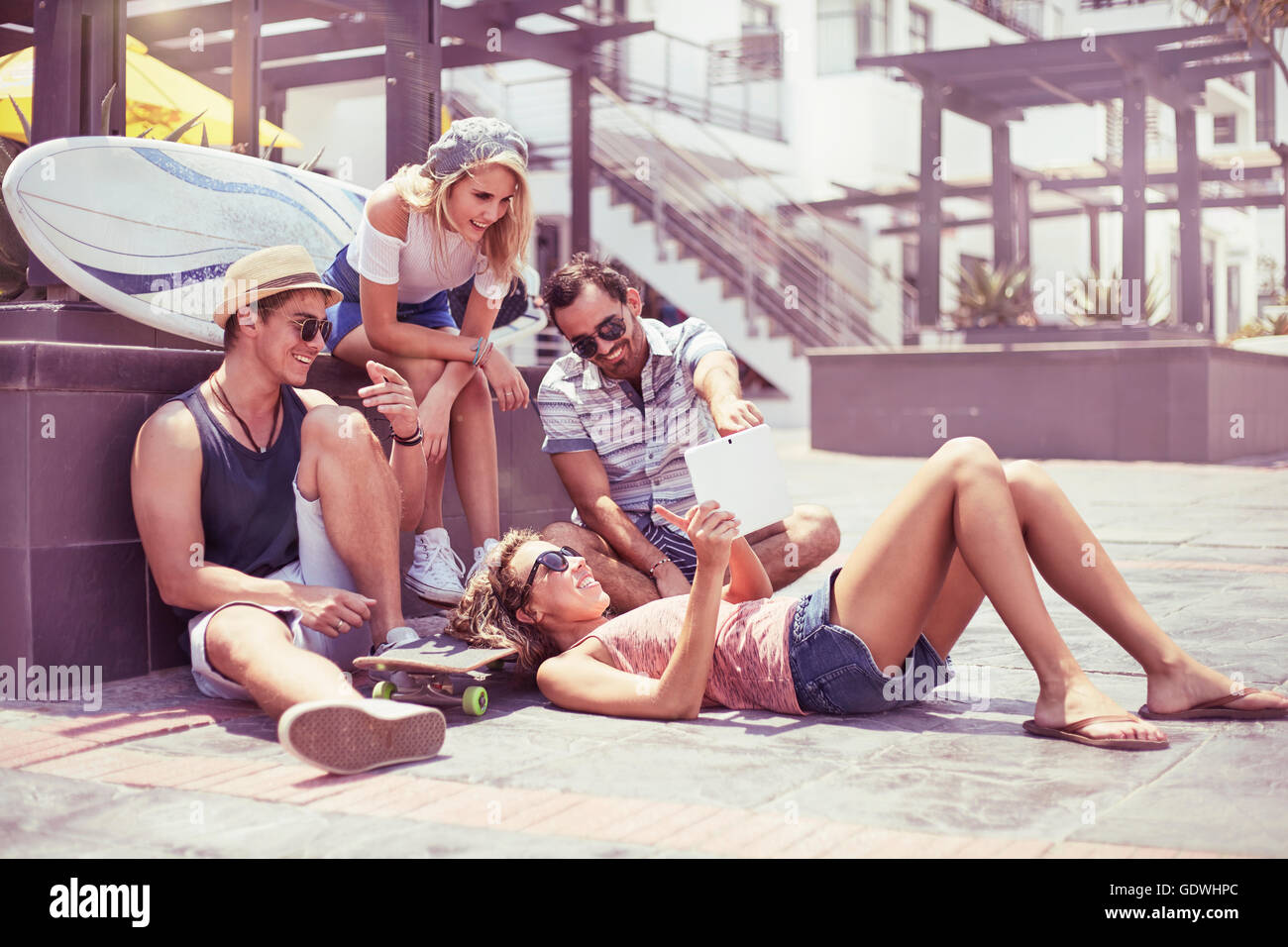 Friends hanging out using digital tablet on sunny sidewalk Stock Photo