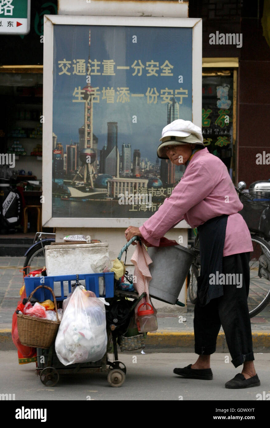 A Chinese woman pushes a cart with things she collected walks on a street Stock Photo