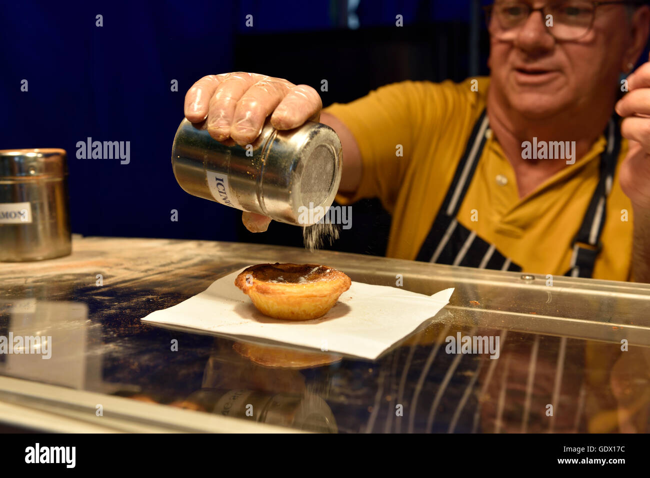 Sprinkling icing sugar on Pastel de Nata custard tart at a food stall during festival UK Stock Photo