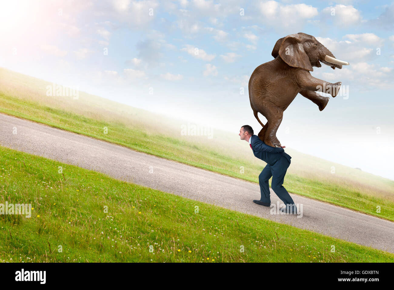 business adversity concept with businessman carrying elephant uphill Stock Photo