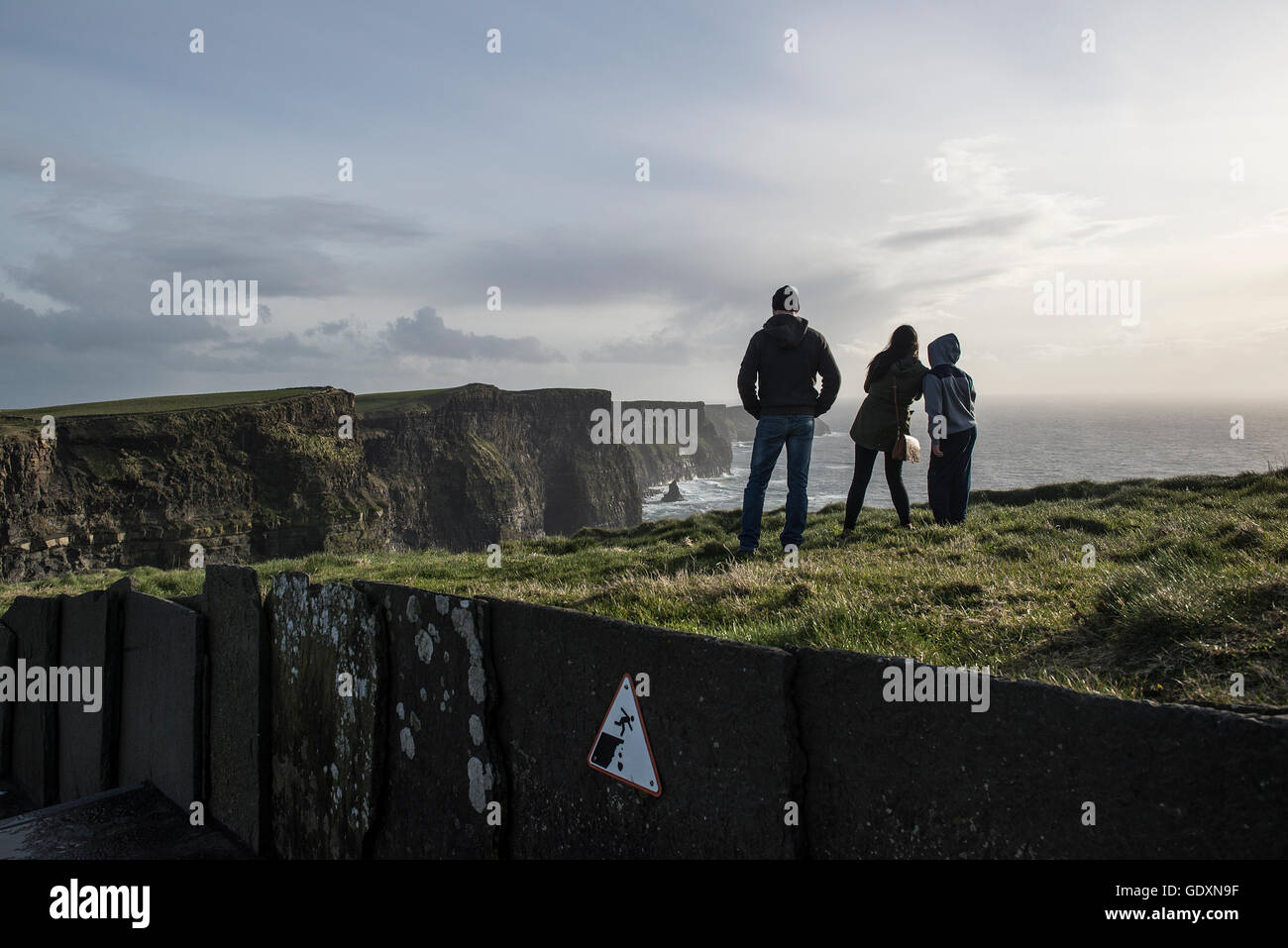 A family of tourists watch the view from the Cliffs of Moher, which are located at the southwestern edge of the Burren region in County Clare, Ireland. They rise 120 meters above the Atlantic Ocean at Hag's Head and reach their maximum height of 214 meters just north of O'Brien's Tower, eight kilometers to the north. Stock Photo