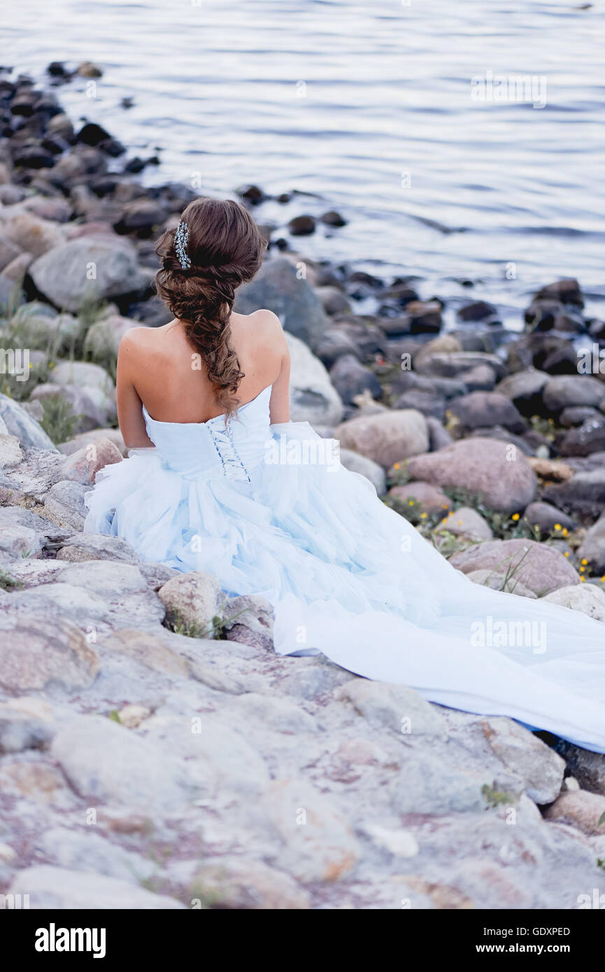brunette in a lush blue dress with beautiful hair sitting on the river ...