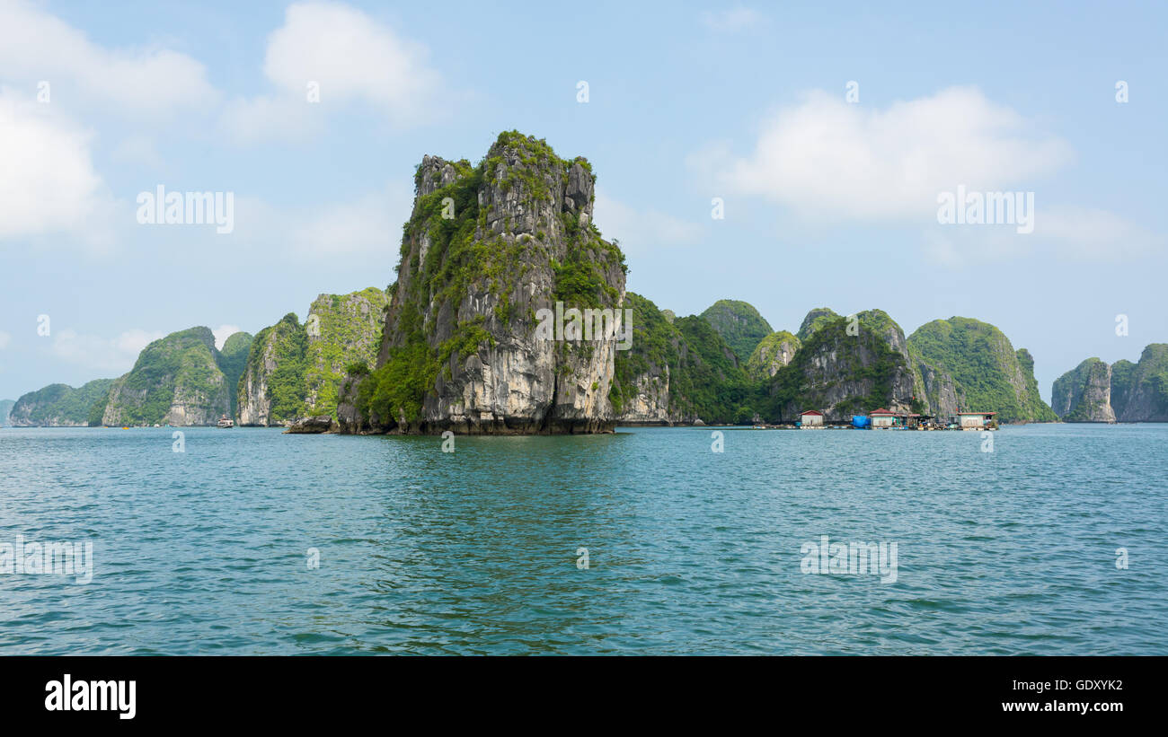 Big cliffs rising from the sea with small floating fishing village next to them, in the beautiful Ha Long bay in North Vietnam Stock Photo