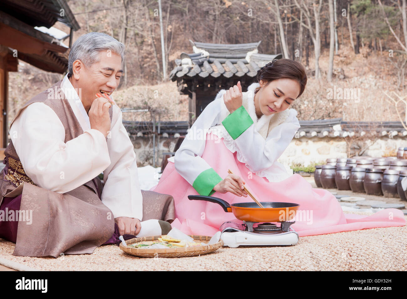 Smiling old man eating traditional Korean food and his tired daughter-in -law cooking Stock Photo