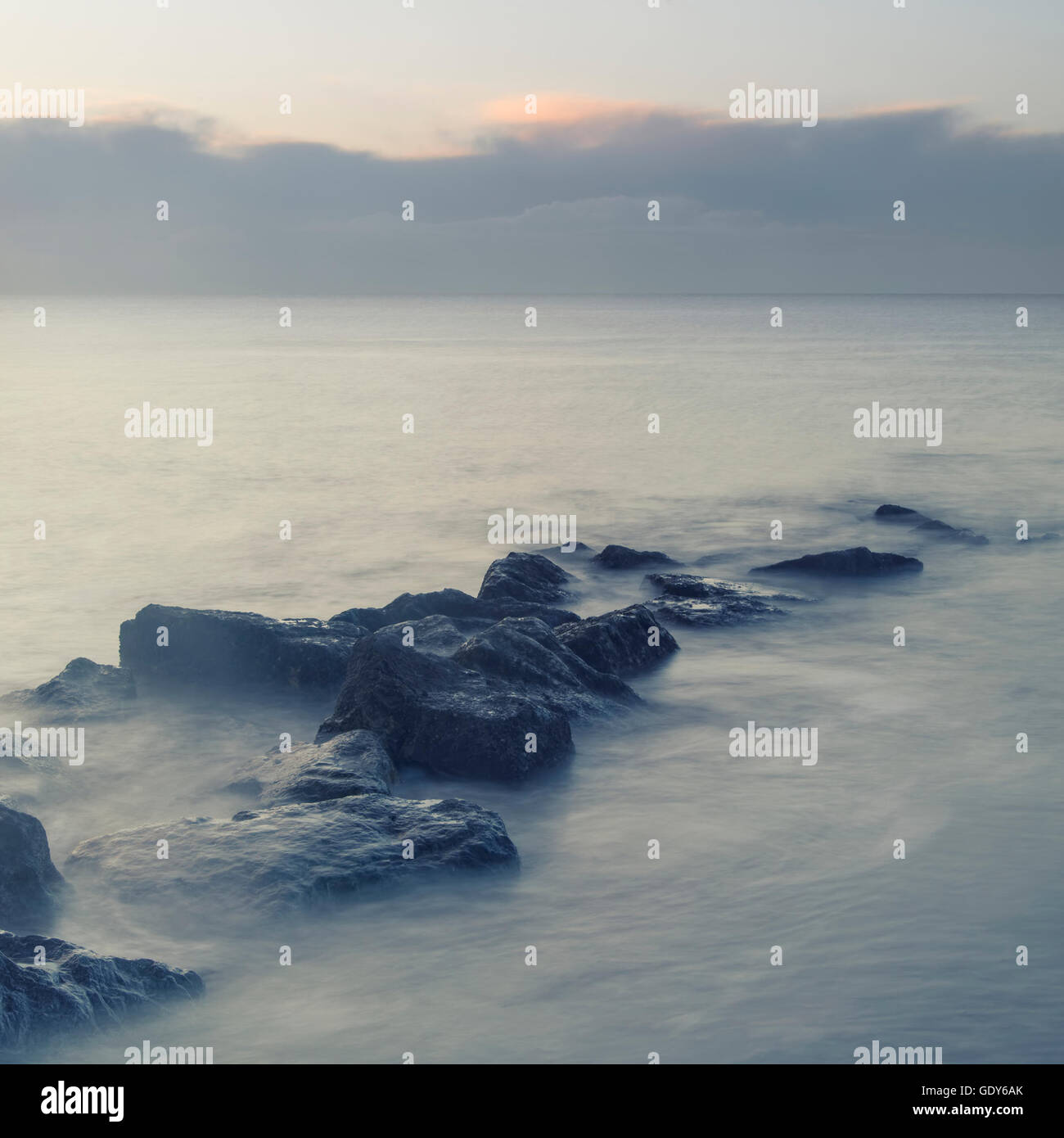 Peaceful cross processed landscape image of calm sea over rocks at sunrise Stock Photo