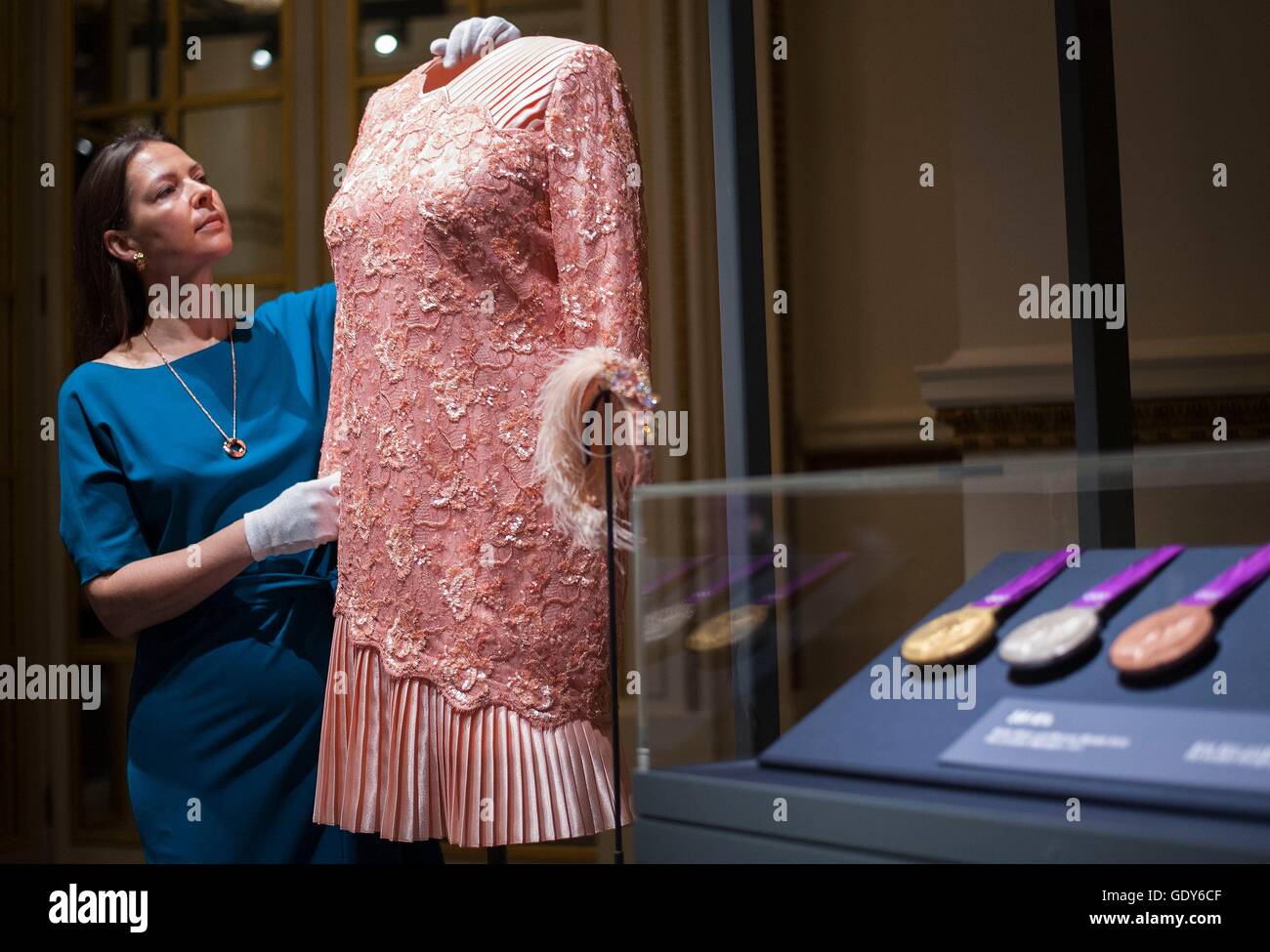 EMBARGOED TO 0001 FRIDAY JULY 22 Curator Caroline de Guitaut adjusts a peach cocktail dress designed by Angela Kelly and worn by Queen Elizabeth II's at the opening Ceremony of the London 2012 Olympic games, during a press preview for Fashioning a Reign: 90 Years of Style from The Queen's Wardrobe, an exhibition at Buckingham Palace in London. Stock Photo